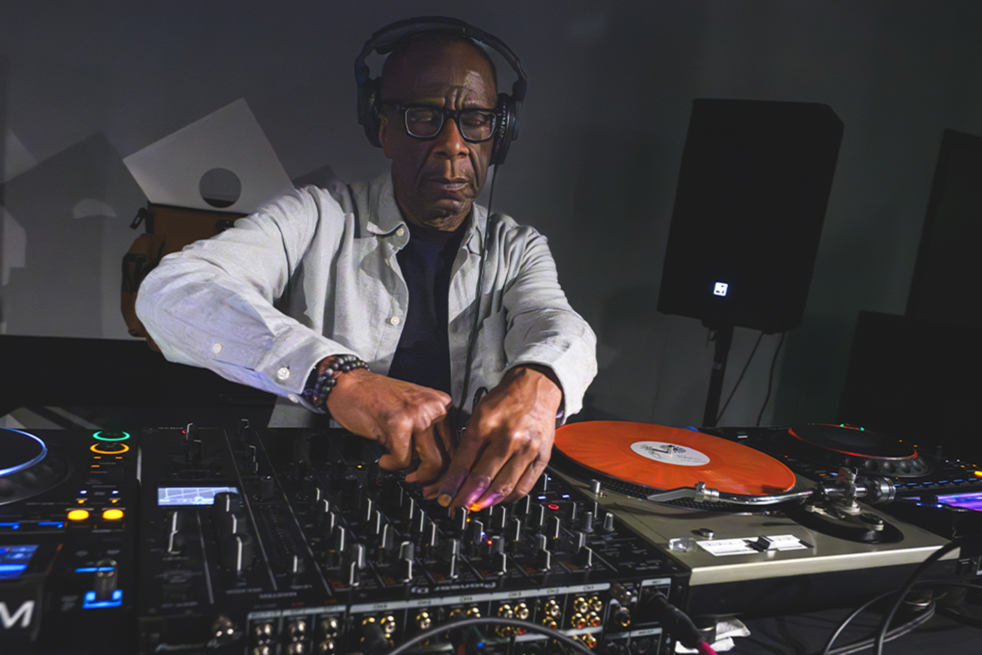 DJ John Collins wearing headphones mixes music behind a sound mixing board.