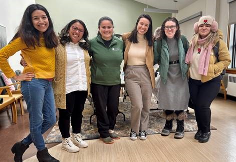 a row of diverse women stand with arms over shoulders smiling