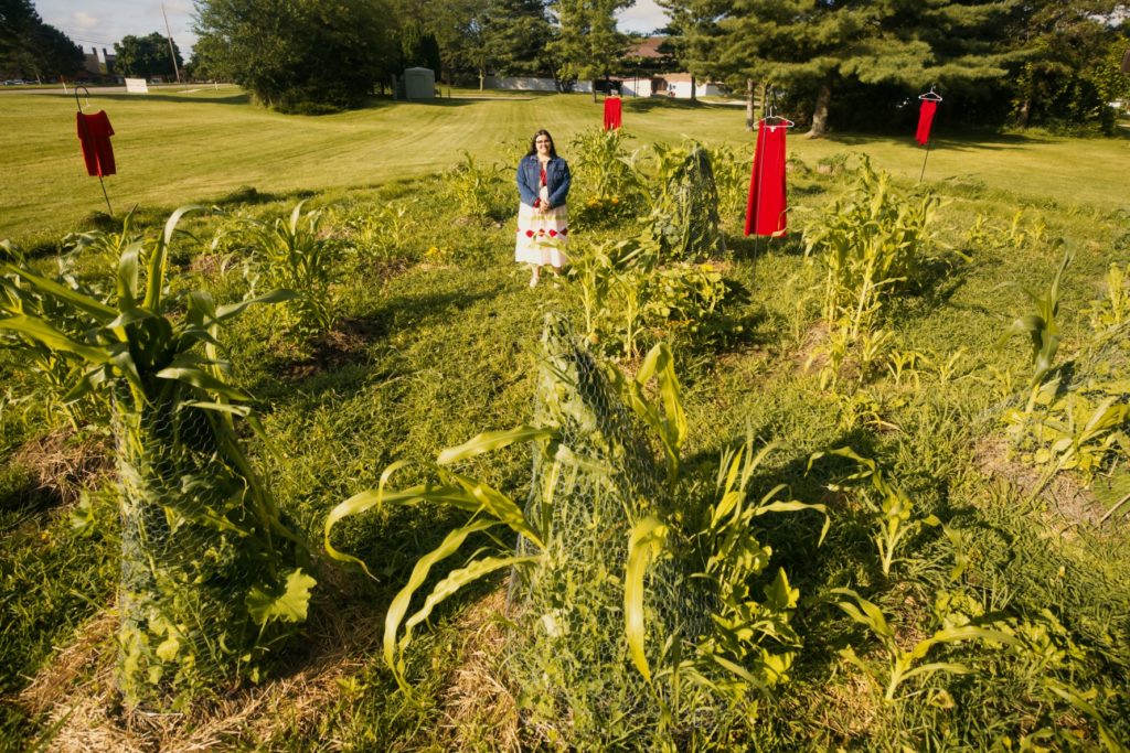 woman stands in garden among four red dresses installed in the background