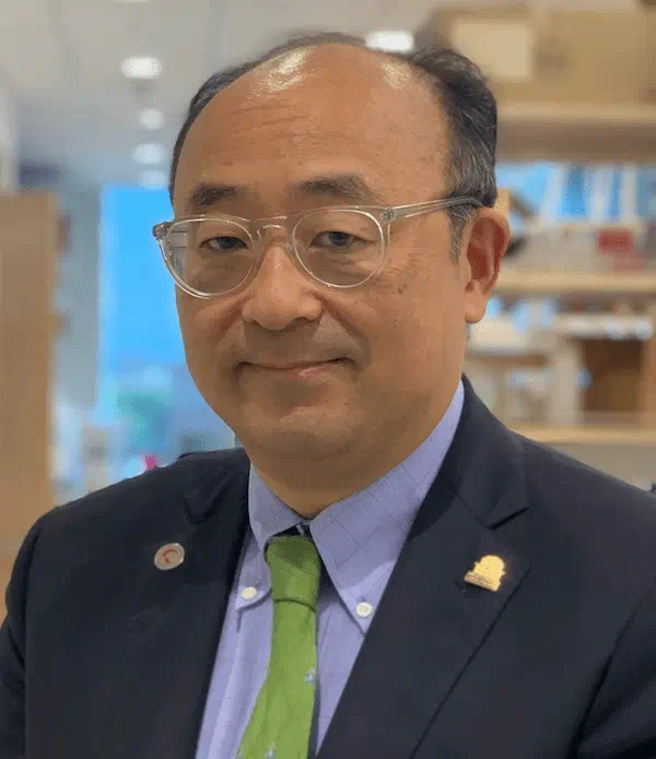 A man in glasses wearing a blue sportcoat over a a purple shirt and a green tiecancer