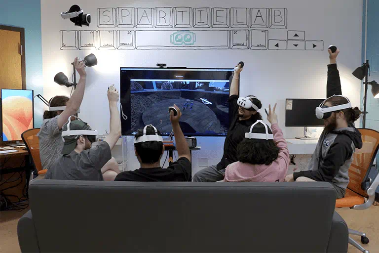 People sitting on a couch using virtual reality headsets while computer animation is on a TV screen.