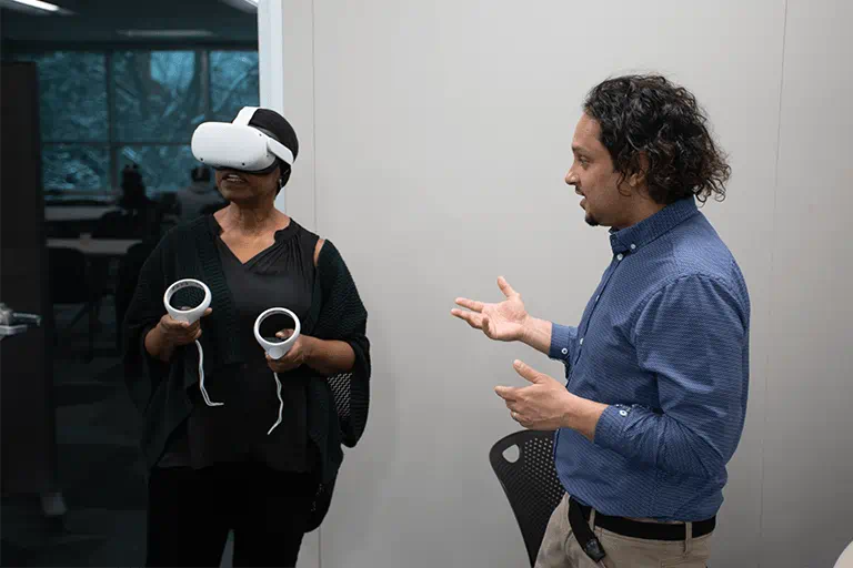 A person uses a virtual reality headset while another person talks with them.