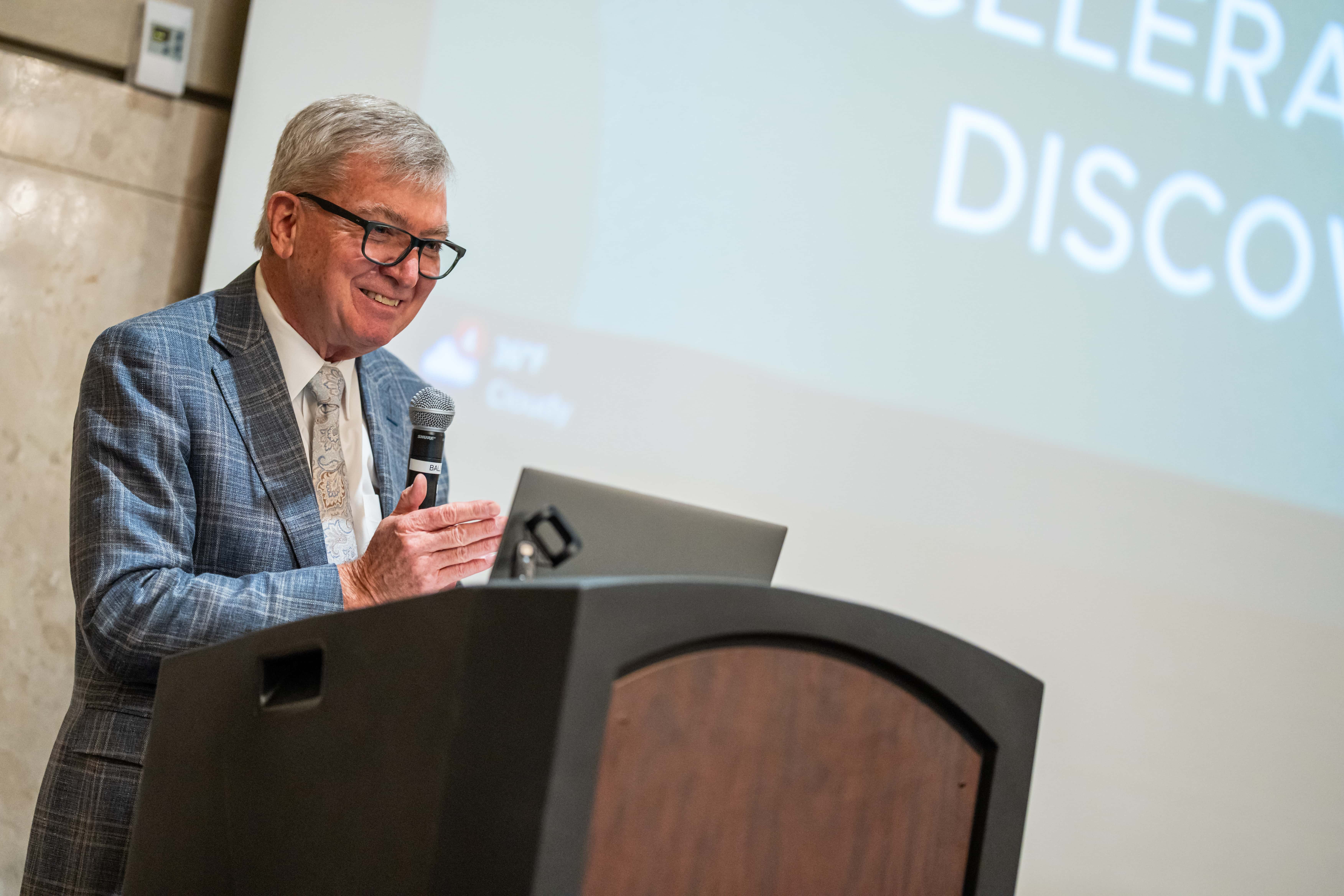 Dr. Doug Gage smiles while holding a microphone and standing at a lectern.