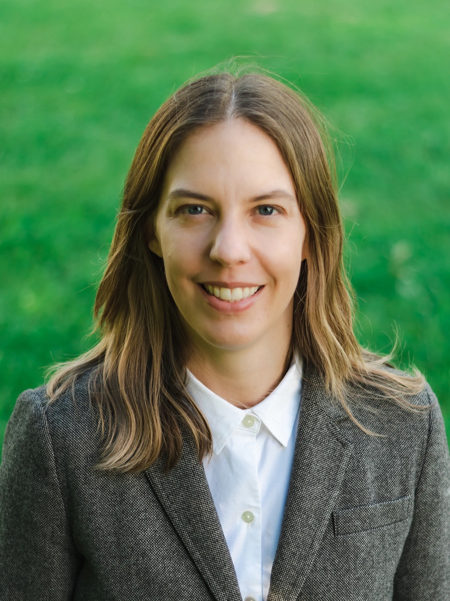 Portrait of a woman smiling wearing a sportcoat and white shirt in front of a grass background