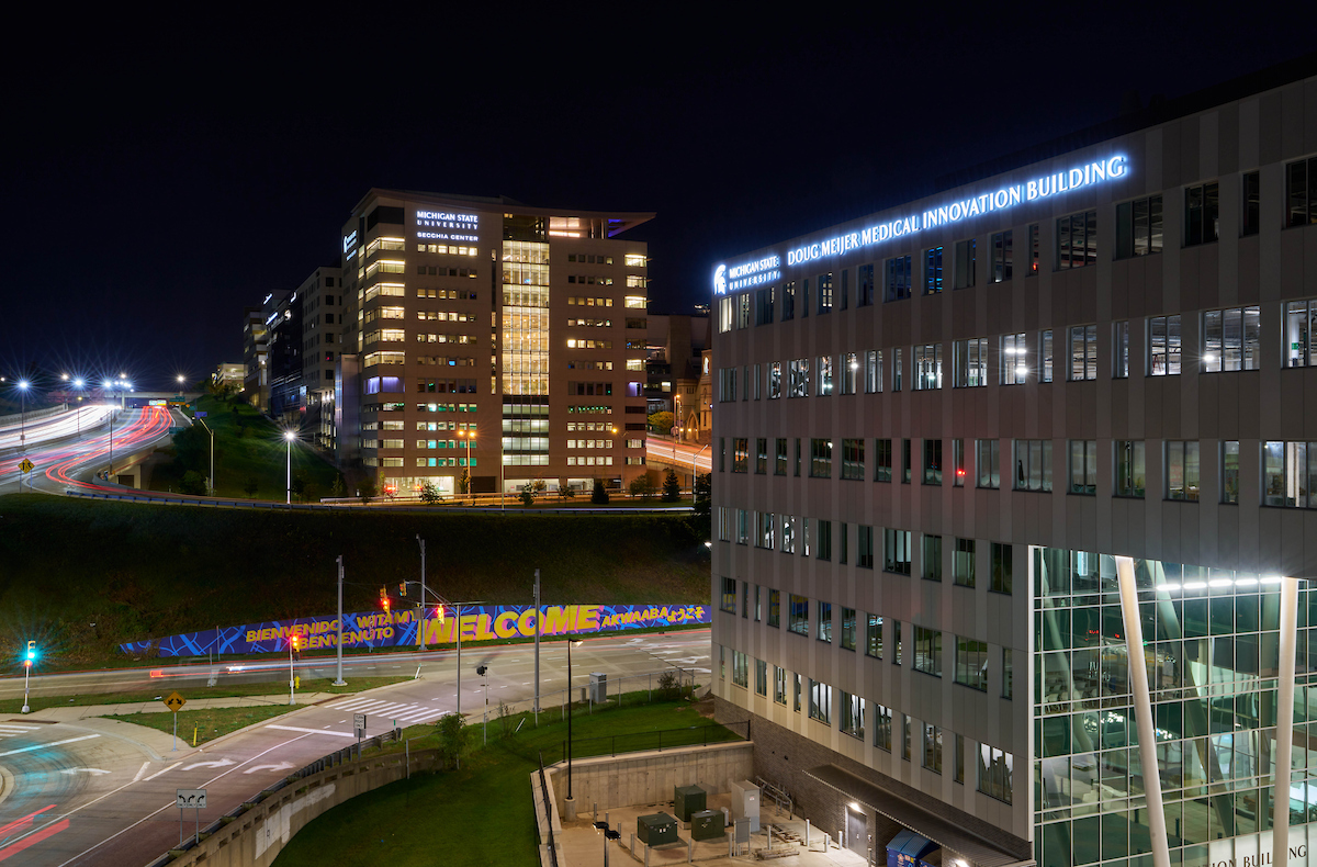 Two buildings on either side of a road with lights on against the night sky. 